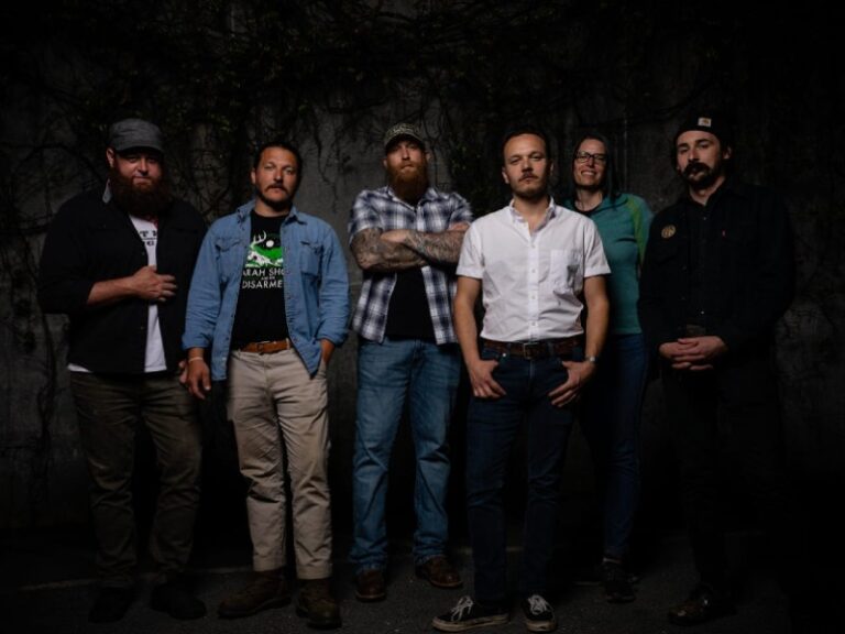 Band members standing in a line in front of a dark background.